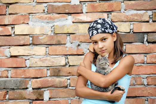 teenage girl outdoor portrait with cat in arms over brick wall