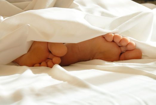 two male feet in white bedding closeup