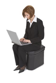 Businesswoman sitting on a pouffe and working on a laptop.