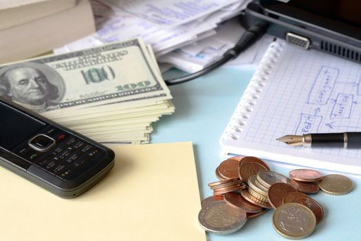 Stack of one hundred dollar bank notes and coins lying on office table with paper