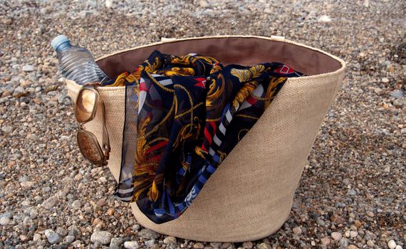 A female beach bag with a bottle of water, sunglasses and a scarf