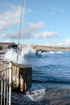waves splashing against a coastal wall during a storm with cars and homes in background