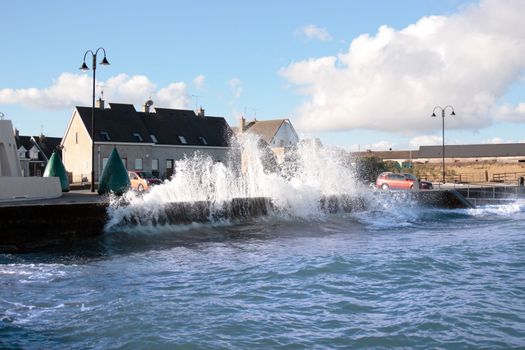 waves splashing against a coastal wall during a storm with cars and homes in background