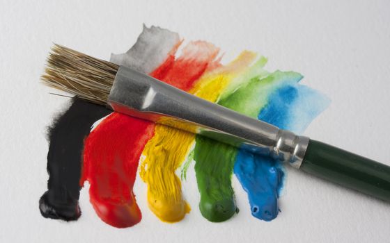 small paintbrush and 5 dabs (black, red, yellow, green, blue) of watercolor paint on white textured paper
