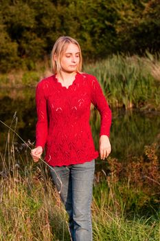 A girl in red pullover in a forest near pond 

