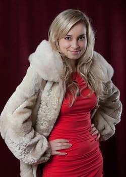 Portrait of the young beautiful girl in a fur coat on a dark background