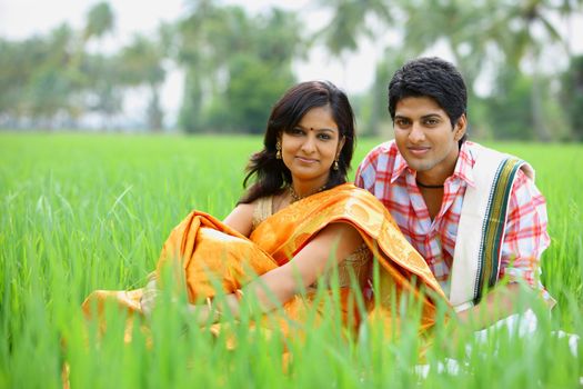 
an asian couple sitting in a paddy field