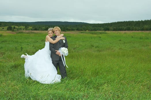 The bride and groom embrace on a green field