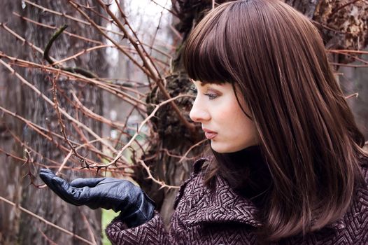 Stylish brunette with gloves and coat near thorns