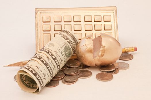 Dollar and change currency next to cracked golden egg with golden calculator and pencil reflect financial jeopardy