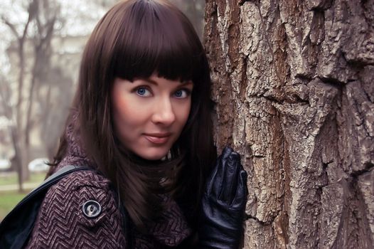Stylish brunette with gloves standing near tree