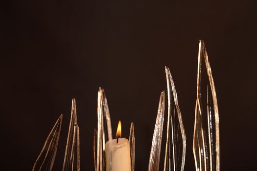 Closeup of few pieces of cracked glass and lighting candle on dark background