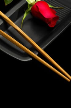 red rose on a japanese black plate with chopsticks over black