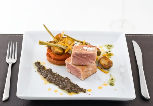 gourmet tuna dish with garnished vegetables and wine.