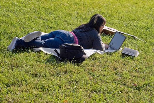 A young student using her laptop computer while laying in the grass on a nice day.