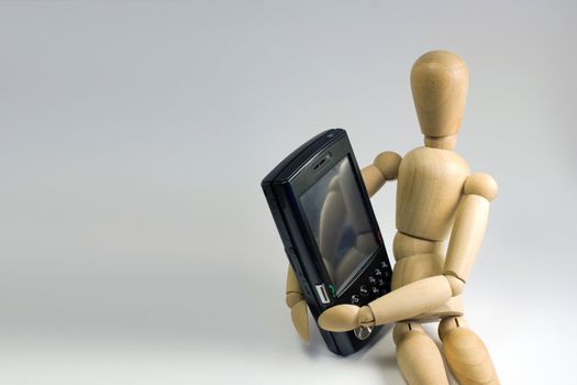 Wooden dummy grasping a mobile smartphone in his arms.