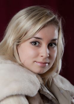 Portrait of the young beautiful girl in a fur coat on a dark background