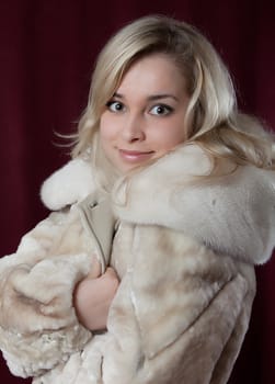 Portrait of the young beautiful girl in a fur coat on a dark background