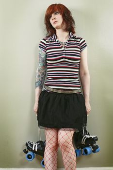 Photograph of a bored roller derby girl holding her skates and waiting against a wall.