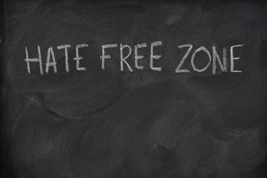 hate free zone text handwritten with white chalk on a school blackboard with strong eraser smudge patterns, copy space