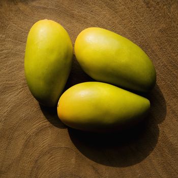 Still life of three wooden mangoes on plate.