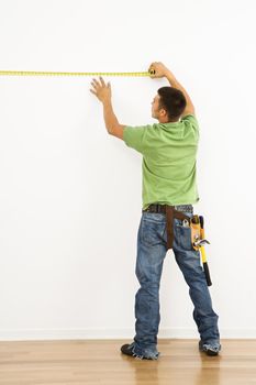 Man wearing tool belt measuring interior wall.