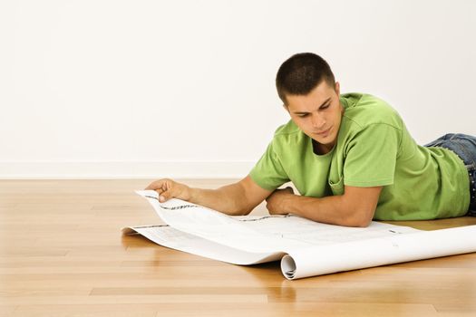 Attractive man lying on floor in home reading house plans.