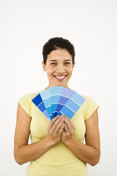 Pretty smiling woman holding paint sample cards in front of white wall.