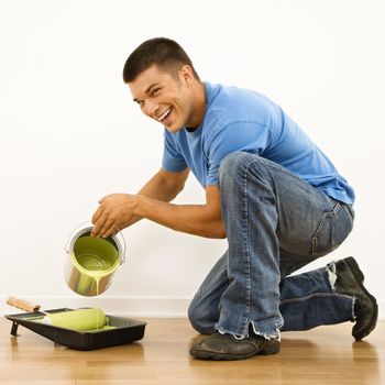 Attractive man smiling and pouring paint into roller pan in home.