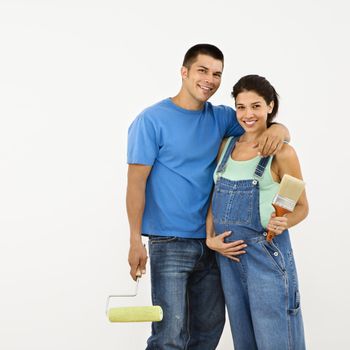 Couple expecting baby holding paintbrushes and smiling.