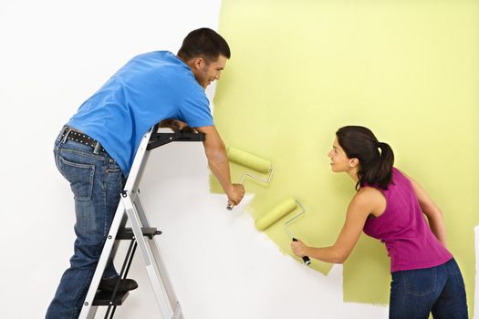 Attractive young adult couple painting interior wall of house.