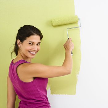 Pretty smiling woman painting interior wall of home with paint roller.