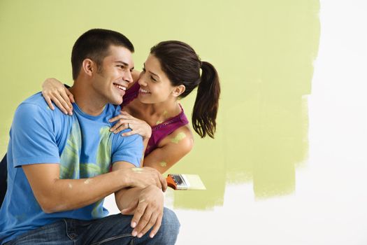 Couple smiling and laughing while painting interior wall of home.