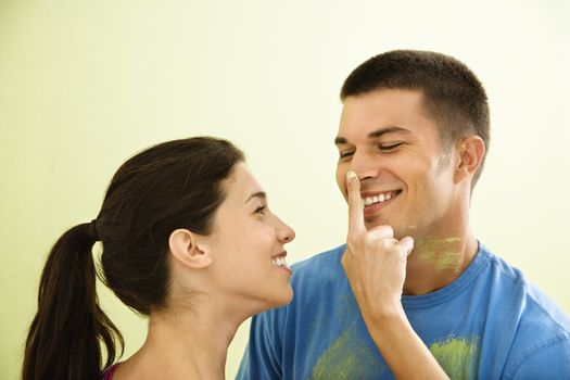 Playful smiling woman putting paint on man's nose.
