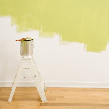 Paintbrush on can on top of step ladder with painted wall.