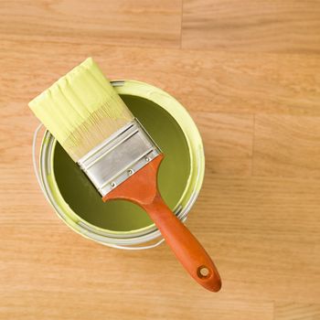 High angle view of paintbrush resting on paint can on wood floor.