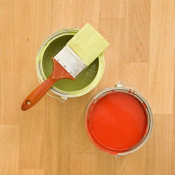 High angle of paintbrush with paint cans on wood floor.