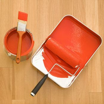 High angle of paint roller in tray with paint can on wood floor.