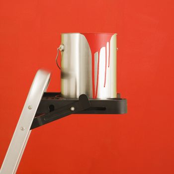 Still life of paint can on step ladder in front of red wall.