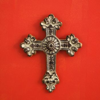 Ornate religious cross hanging on red wall.