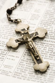 Crucifix on rosary lying on open Bible.