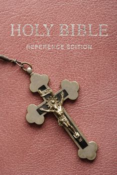 Crucifix lying on cover of closed Holy Bible.