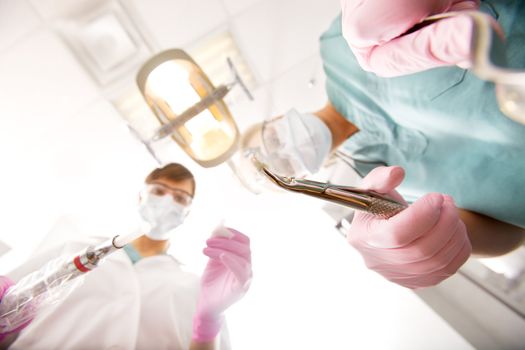 A dentist and assistant pulling teeth from the viewers mouth, focus on the pulled tooth