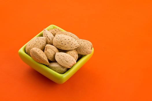 Almonds in a bowl, with orange background.