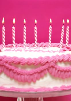 Lit birthday candles on a pink cake are waiting to be blown out as a wish is being made.