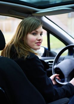 Blond teenage girl sitting in a car behind the wheel 