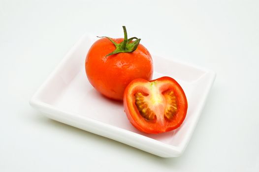 Tomoato on plate, white background, with drops of water.