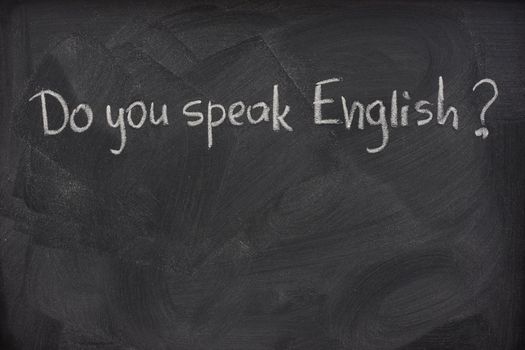 do you speak English question handwritten with white chalk on a blackboard with eraser smudges