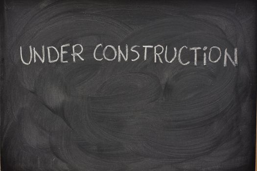 under construction phrase handwritten with white chalk  on a blackboard with eraser smudges and copy space below