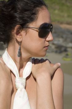 A young brazilian brunette wearing a white tie and aviator sunglasses on the beach.